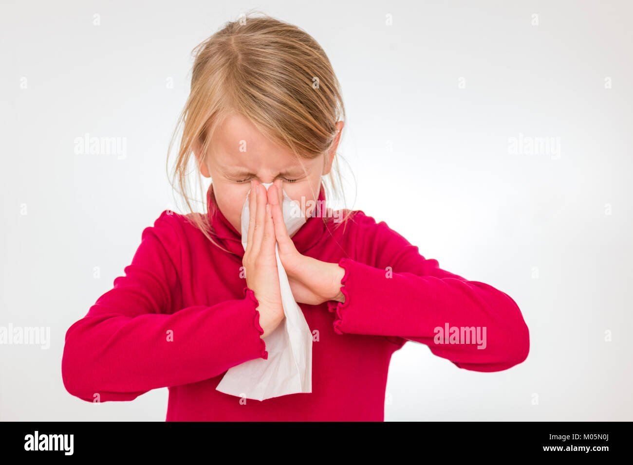 A girl is biting into a white handkerchief. She is 7 years old and wears a red pullover. Stock Photo