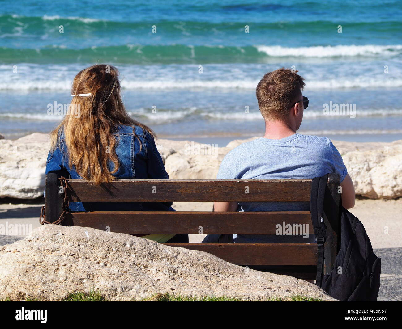 two Friends sitting on a bench on the beach promenade on a perfect clear day watching the sea Stock Photo