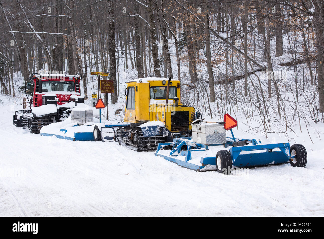 Two snowmobile trail groomers, a yellow Bombardier and a red Pisten Bully, parked on the Perkins Clearing road in the Adirondacks. Stock Photo