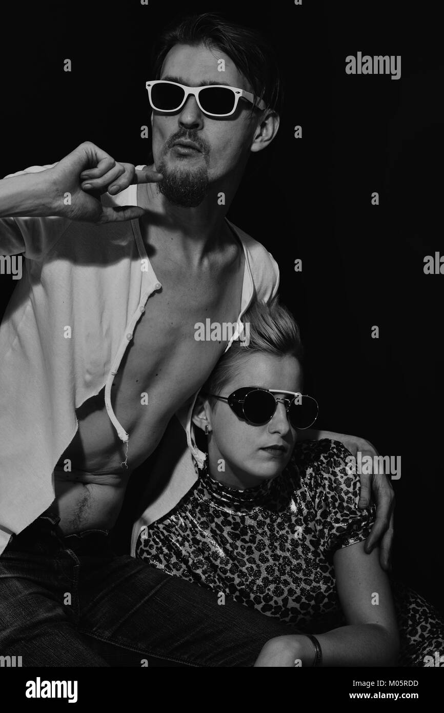Stylish young man and woman wearing sunglasses on a black background ...