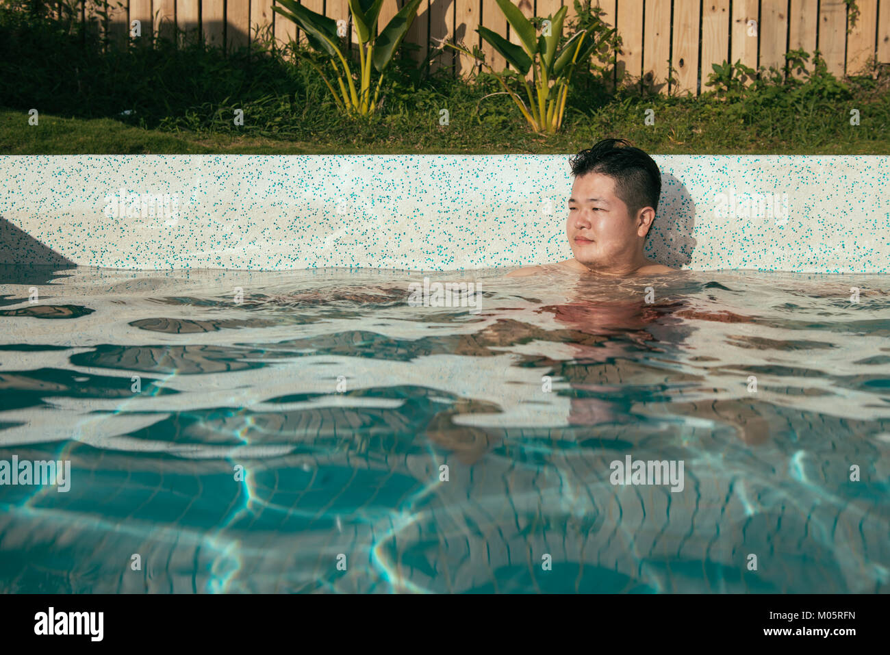 smiling young man sitting in swimming pool relaxing and making daydreaming to enjoying summer vacation. Stock Photo