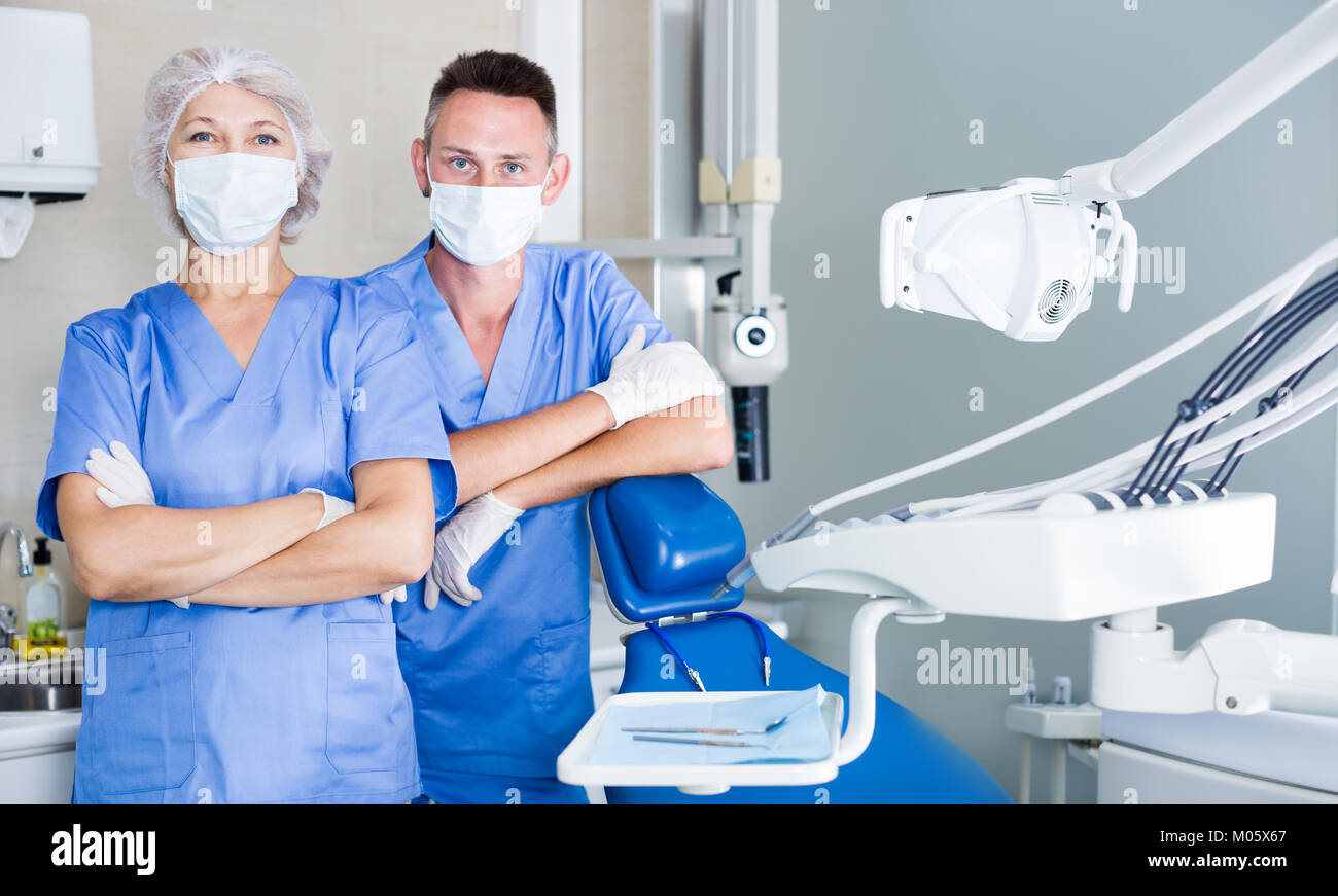 Two professional confident dentists posing near a dental chair in clinic. Focus on both persons Stock Photo