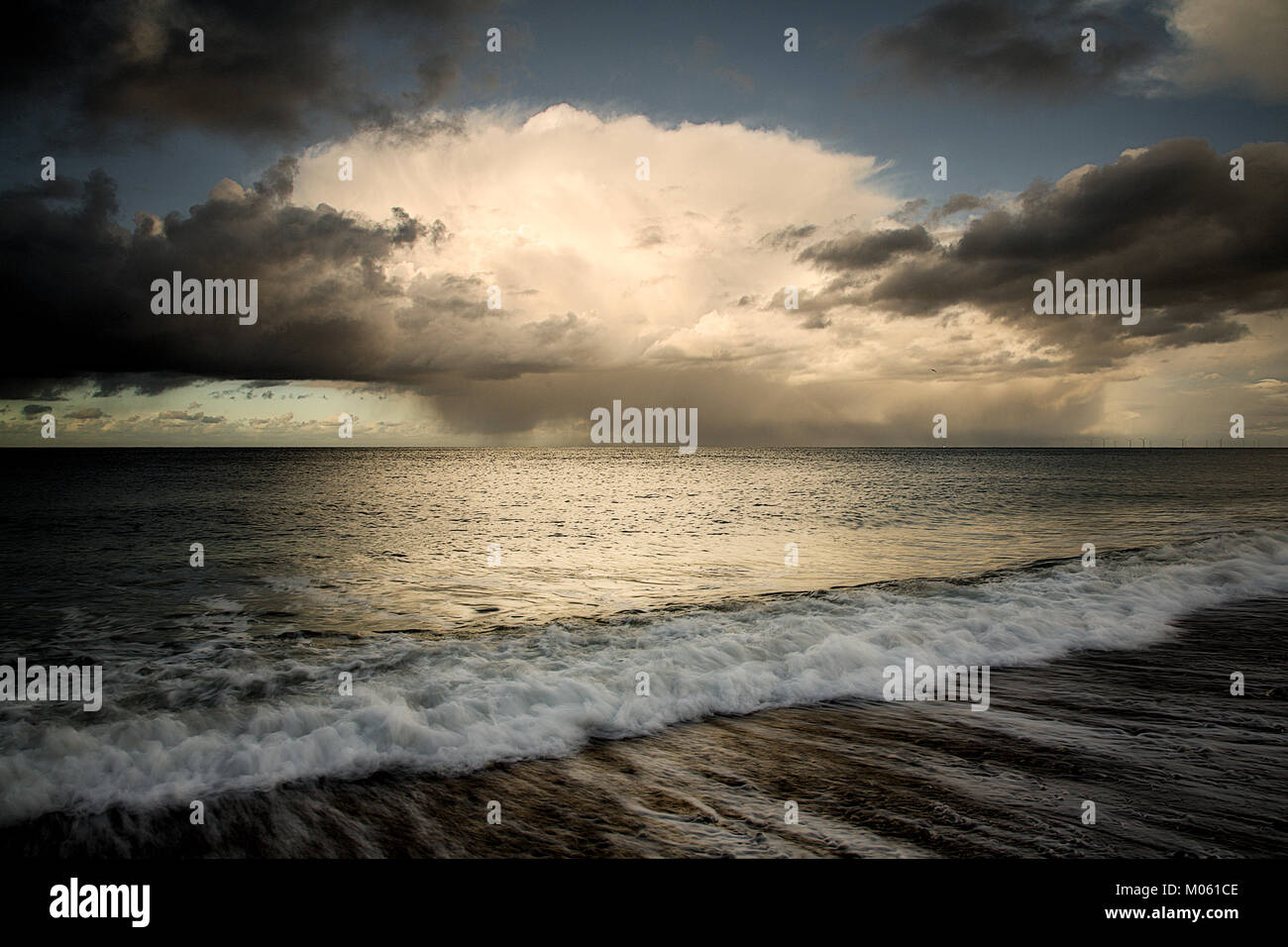 Storm clouds over the Irish Sea with a wave breaking on the beach at ...