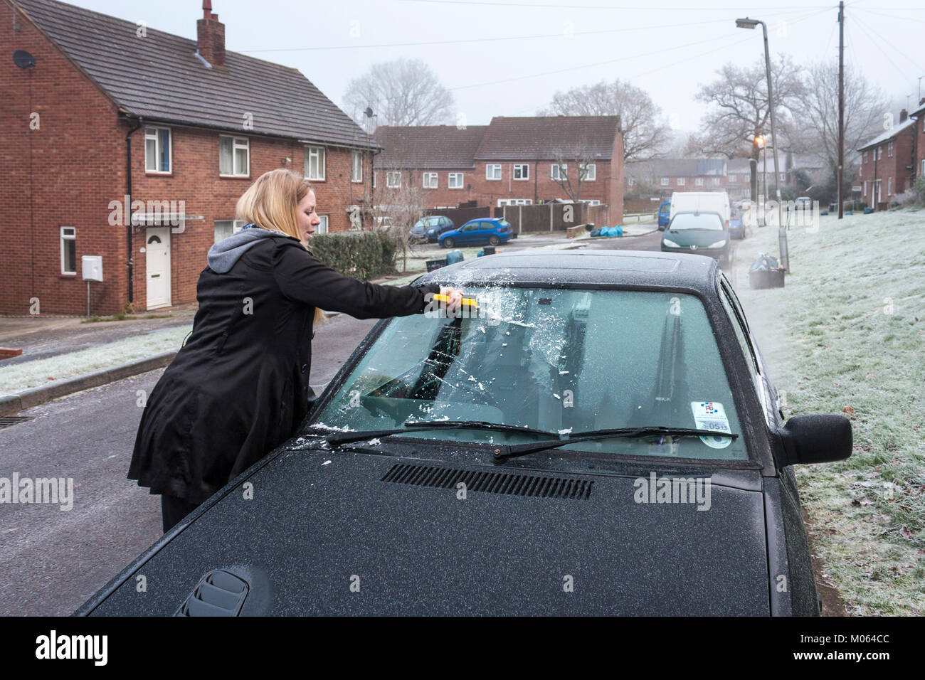 Woman scrapes frost from car windscreen in winter Stock Photo