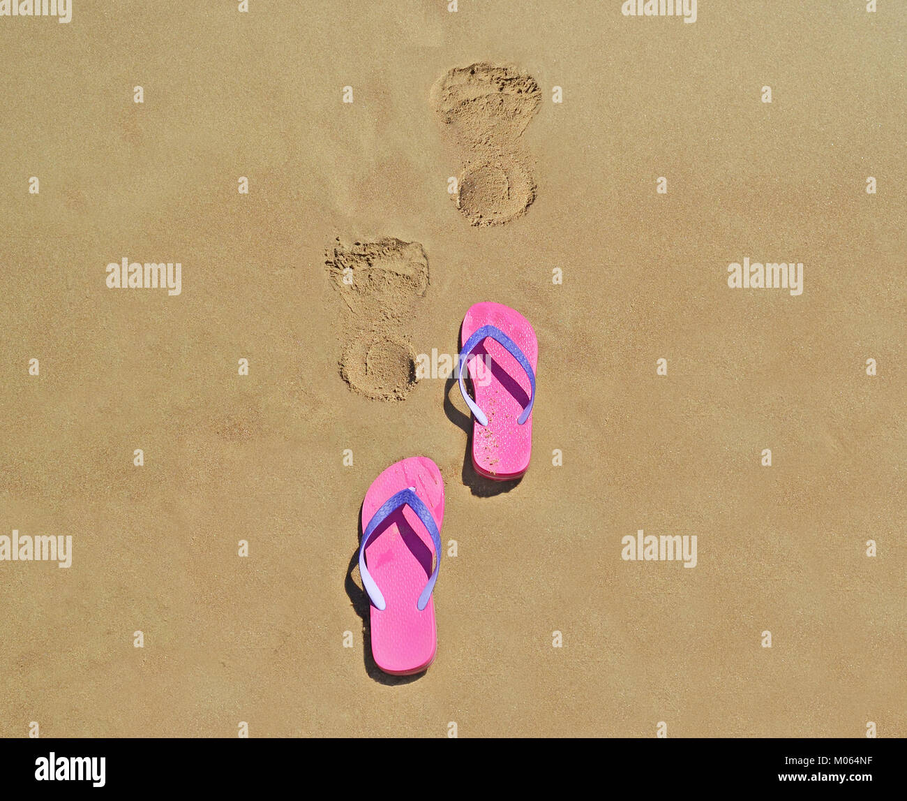 summer flip flops on the beach with footsteps on sand - summer vacation