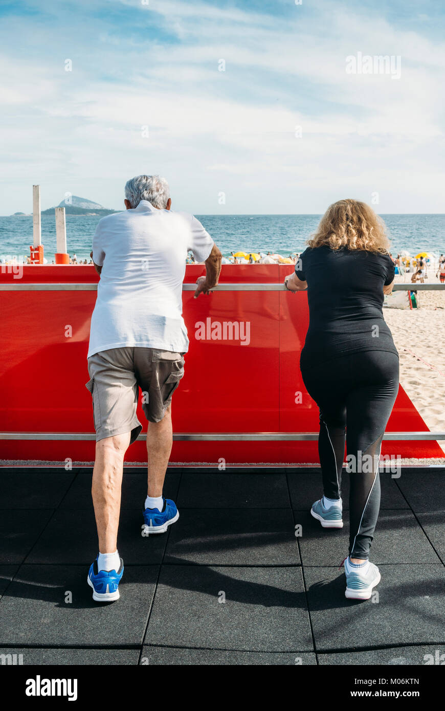 Model Released - Mature heterosexual couple stretching hamstrings on beach-side gym Stock Photo
