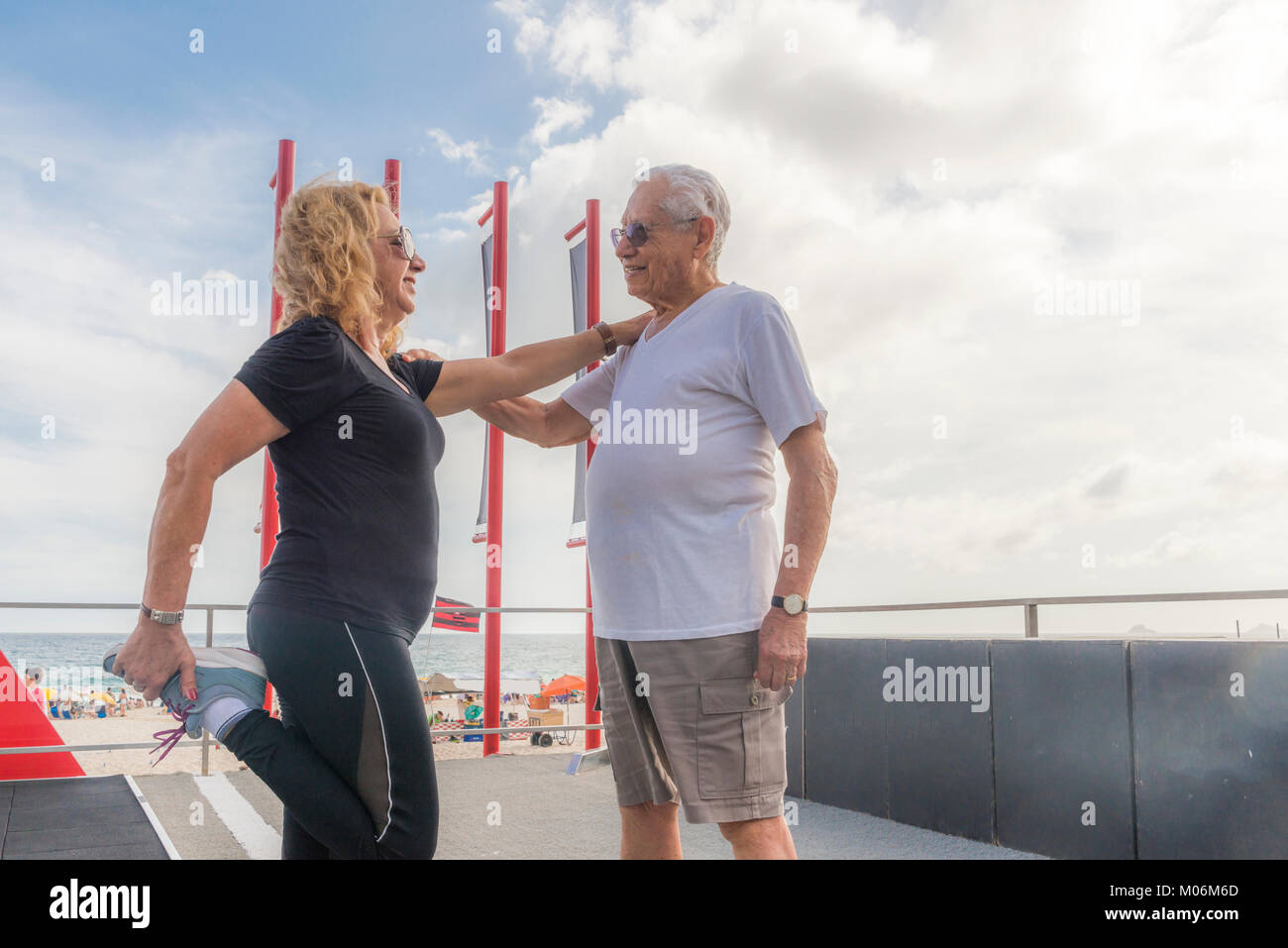 Model Released - Mature heterosexual couple exercising together. Man supporting woman while she stretches her quadriceps Stock Photo