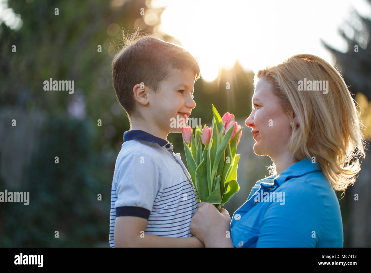 Little son gives bouquet of tulips to mom at Mother's day in sunset, looking to each other Stock Photo