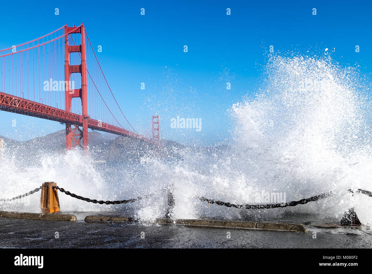 Golden Gate Bridge view framed by huge waves crashing over a sea wall below the bridge. Stock Photo