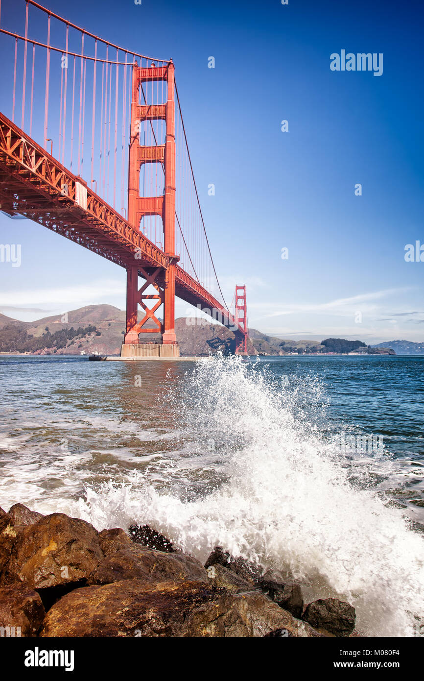 Golden Gate Bridge, San Francisco. Viewed from the boulders below with splashing waves in the foreground. Vertical Stock Photo
