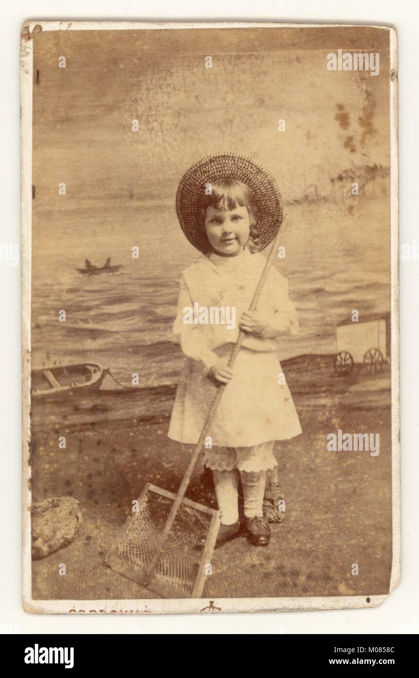 Original characterful and charming Victorian studio Carte de Visite (CDV) portrait of child (girl or boy as they were dressed the same in these times) holding shrimp net prop, seaside backdrop, from the studio of photographer Alfred Goodchild, Redcar, North Yorkshire, England, U.K. dated 1886 Stock Photo