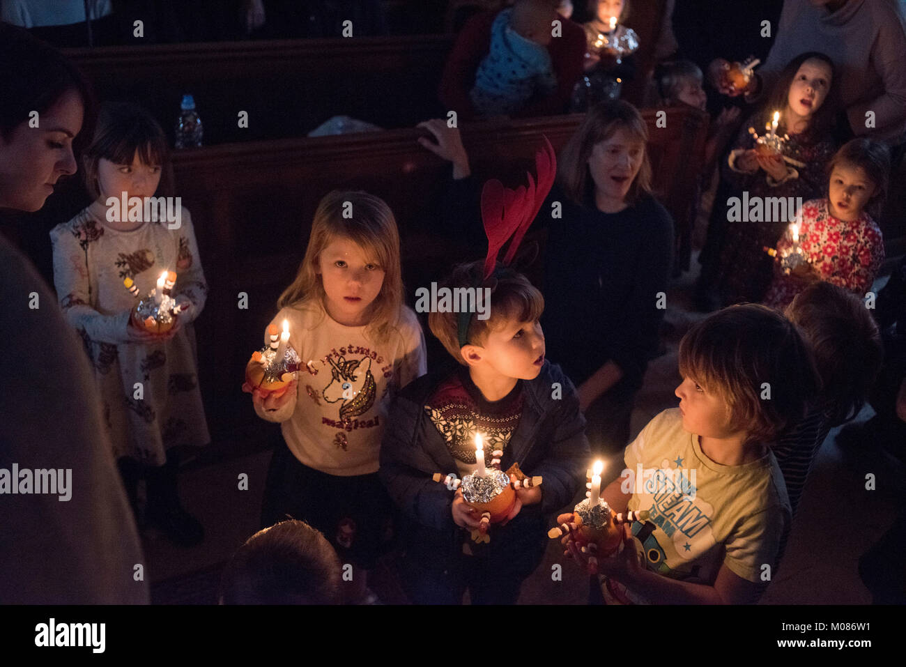 Children process at a Christingle event at St Mary's church Walthamstow, London. Xmas Eve 2017.  A Christingle is a symbolic object used in the Advent services of many Christian denominations. Christingle means 'Christ Light' and is used to celebrate Jesus Christ as the 'Light of the World'. Used primarily for Advent and Christmas, it is also used for Epiphany.  Made uses orange and sweets. Stock Photo