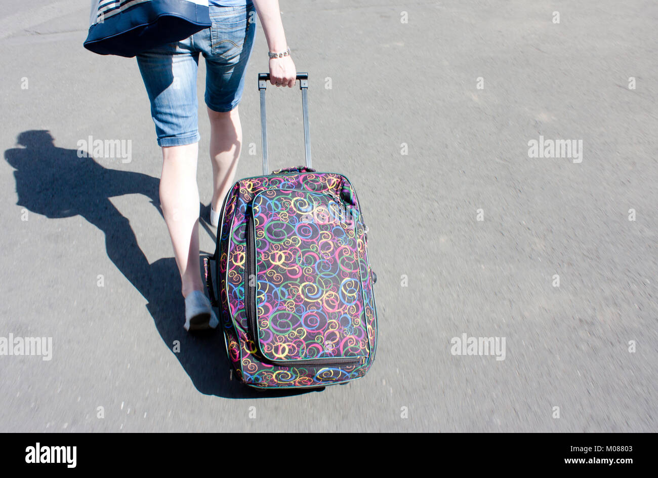 Belgrade, Serbia - September 17, 2017 : Young woman in bermuda jeans shorts with rolling luggage wheeled suitcase walking the city streets Stock Photo