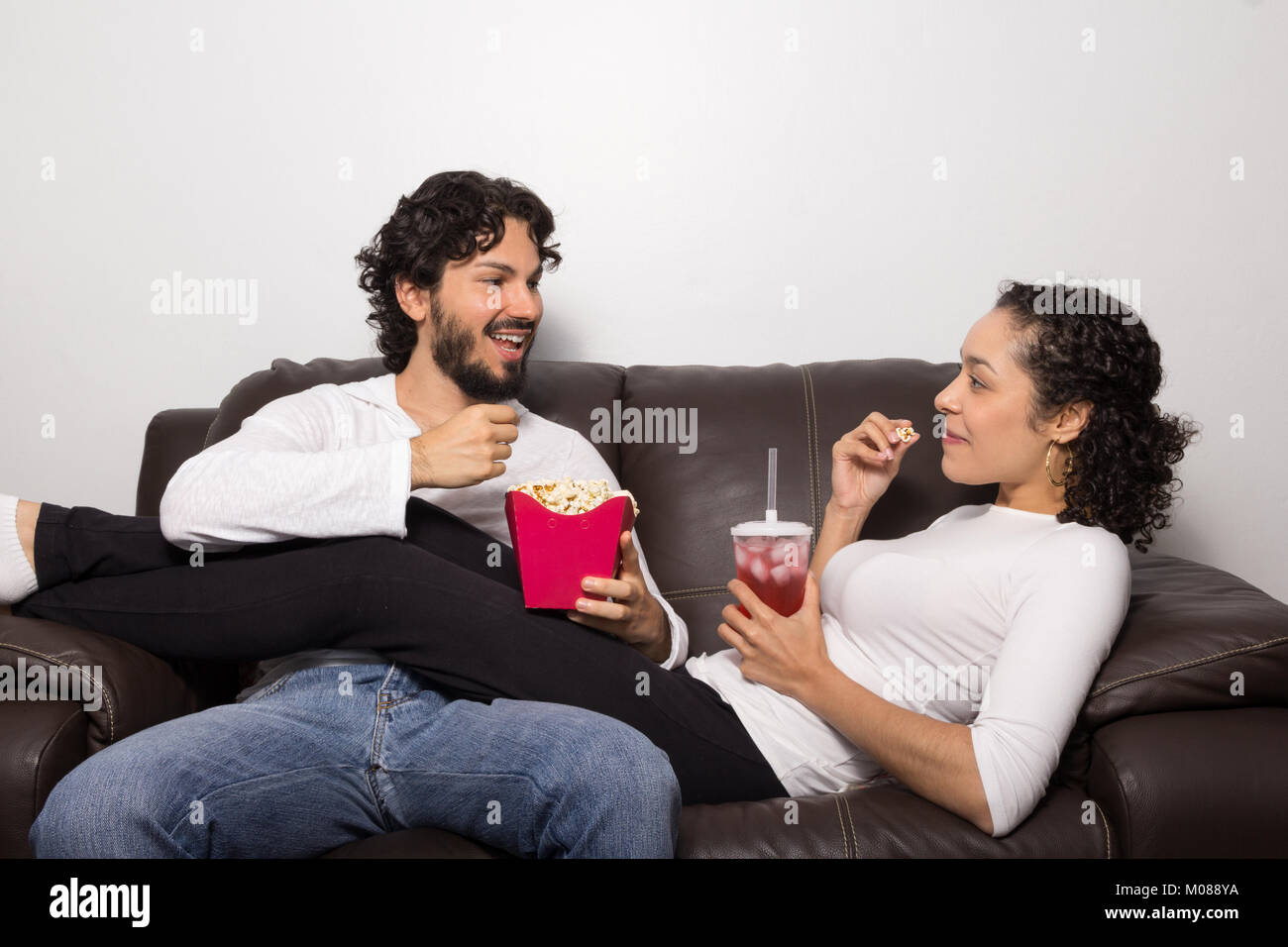 Beautiful couple is eating popcorn and talking. They are on the living