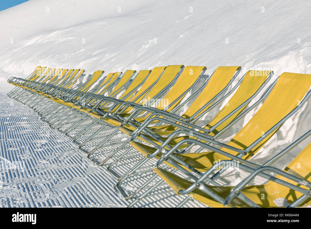 Yellow sun loungers on the slope Dolomites, ski are.. Empty ski slope in winter on a sunny day. Prepare ski slope. Val di Fiemme Stock Photo