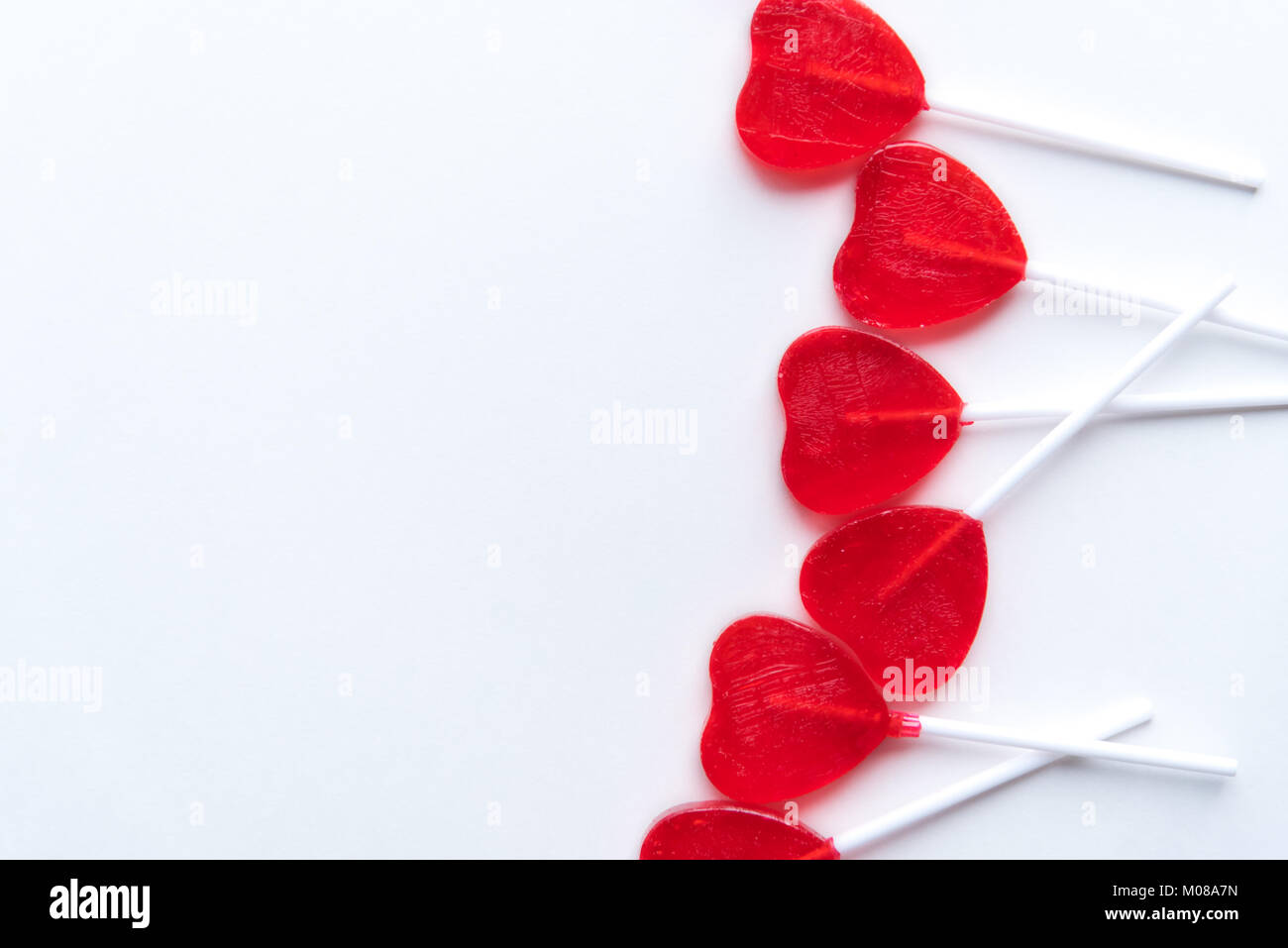 Red heart shaped Valentine lollipops scattered across right side of white background Stock Photo