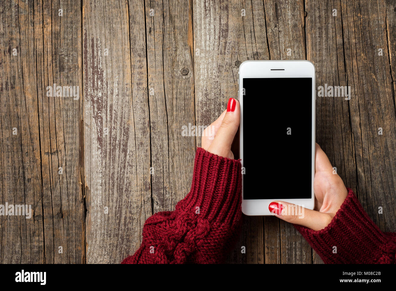Female hands in warm sweater holding white smart phone Stock Photo