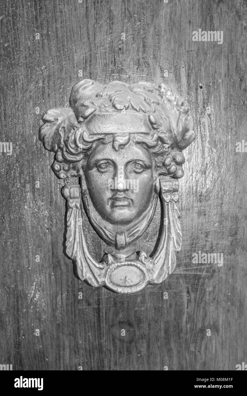 Close-up, isolated shot of a vintage door knocker with face and fancy head piece, mounted on an aged wooden door, in black and white, in Mexico Stock Photo