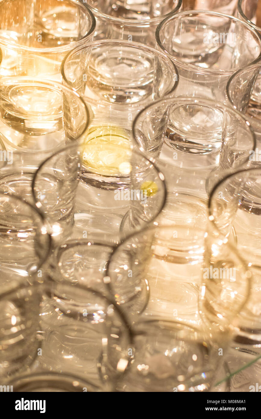 Array of shot glasses on white table - metallic colors. Glasses side by side and reflecting into each other. Stock Photo