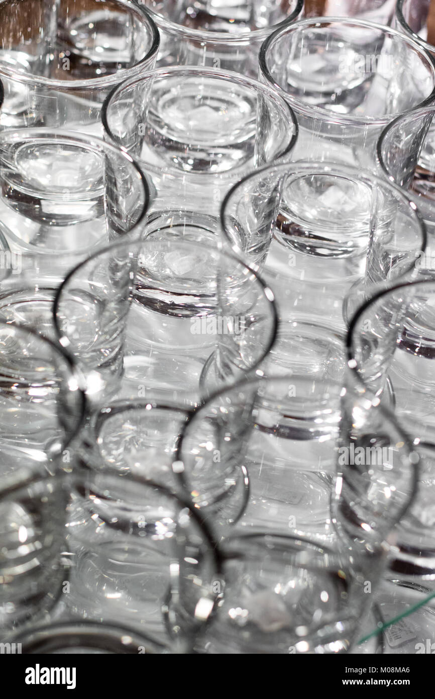 Array of shot glasses on white table - metallic colors. Glasses side by side and reflecting into each other. Stock Photo