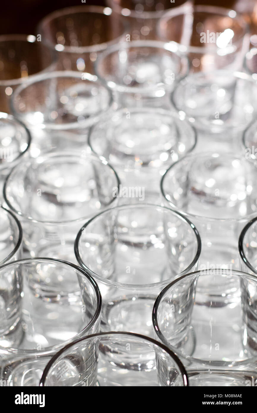 Array of shot glasses on white table - metallic colors. Glasses side by side and reflecting into each other. Stock Photo