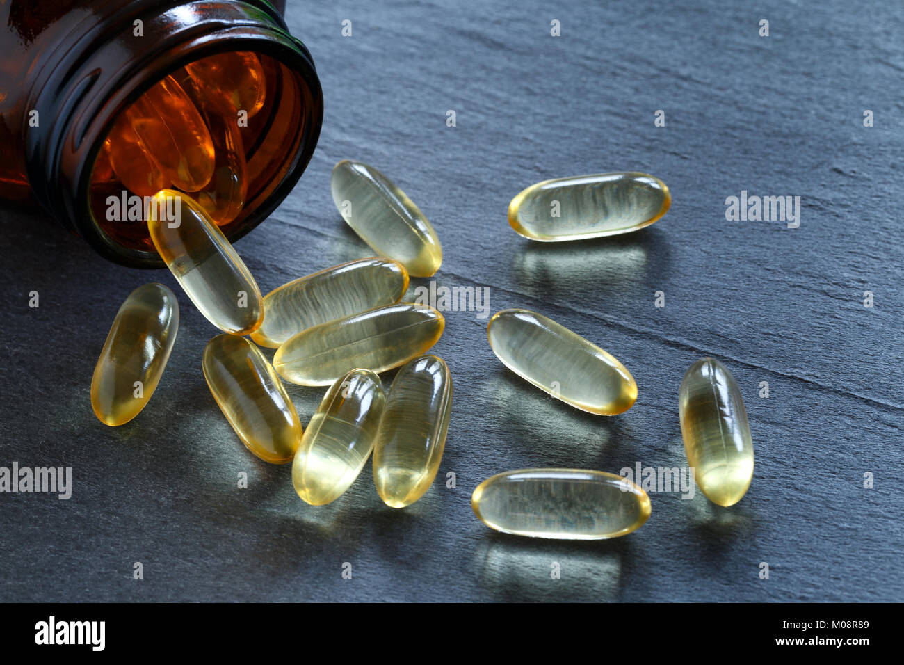 Vitamine D gel capsules with glass supplement bottle against a dark slate background Stock Photo