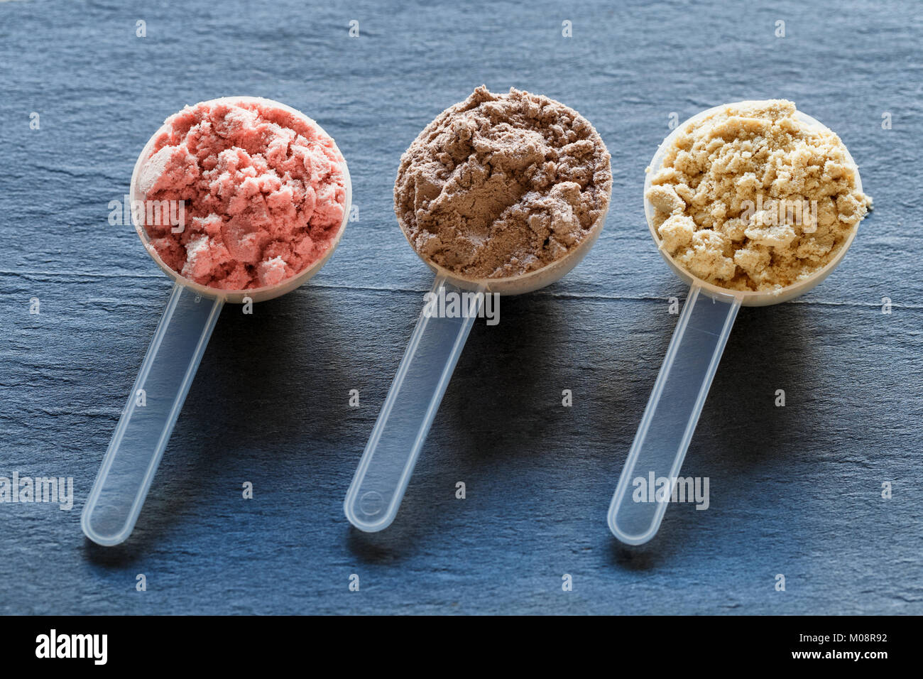 Plastic measuring spoons filled with whey protein powder against dark