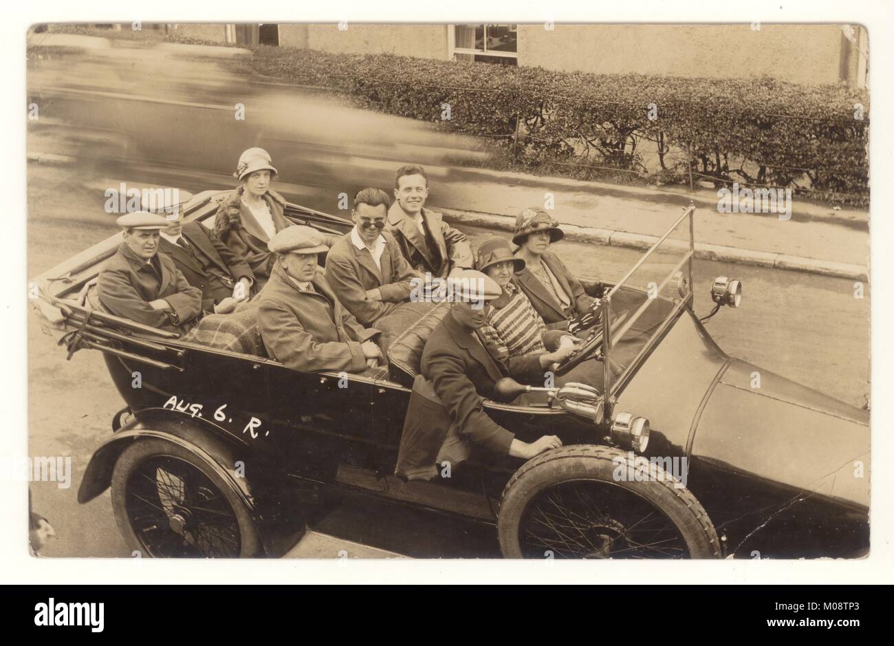Original real photographic postcard of happy group of people, men and women, in a small charabanc, fashionable cloche hats, flat caps .Driving on a summer excursion in August, speed blur, circa 1927,  U.K. Stock Photo