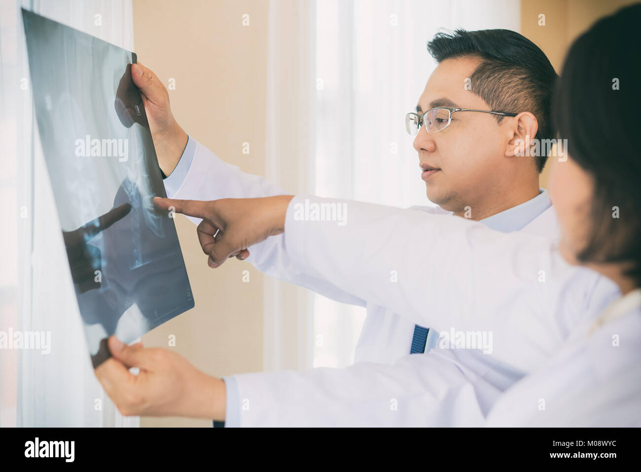 Two Doctor talking and examining x-ray film about result and background blur operating room with X-ray medical scan at hospital. Stock Photo