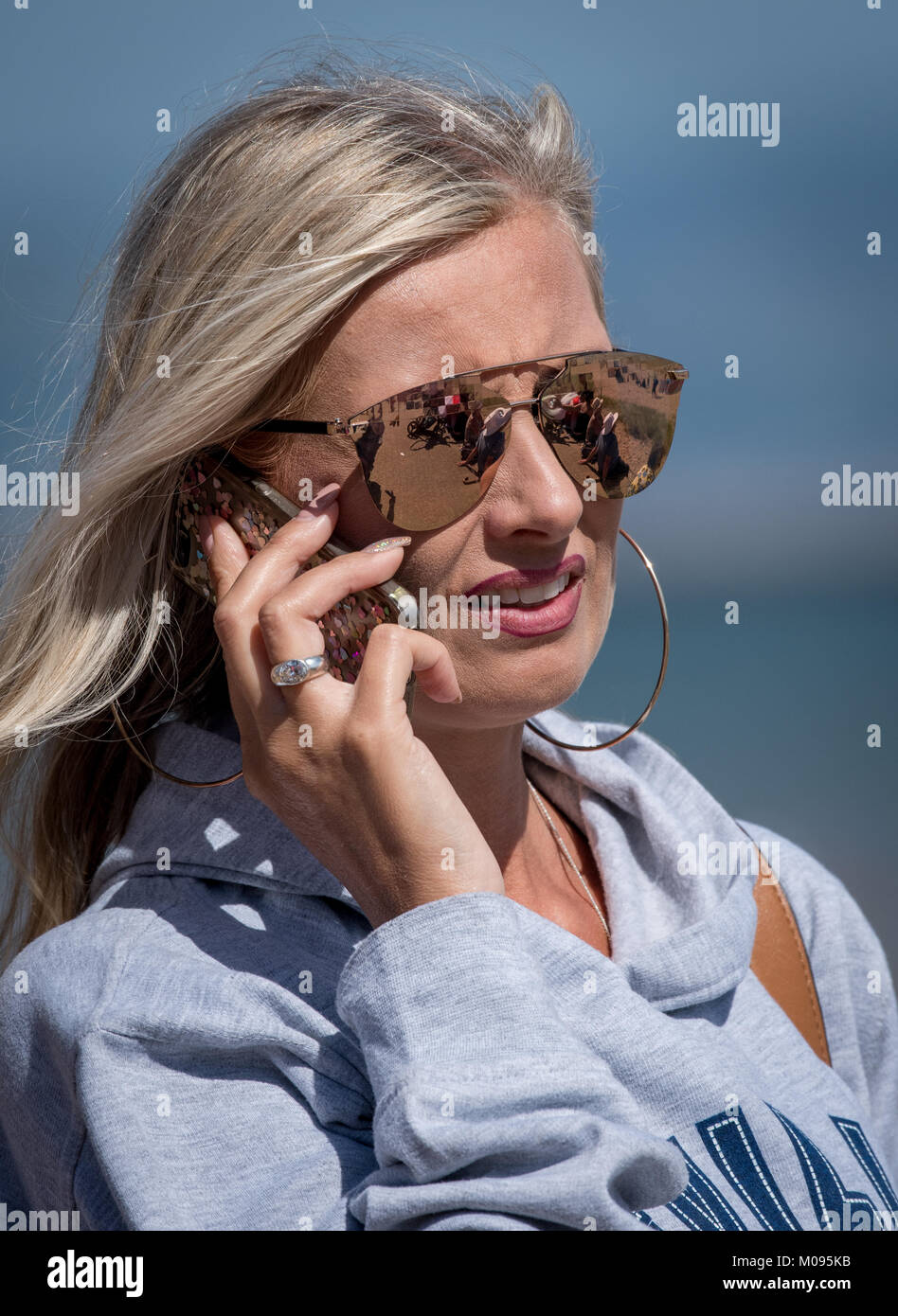 Blonde Highlighted Girl wearing shades, talking whilst on her mobile. Stock Photo