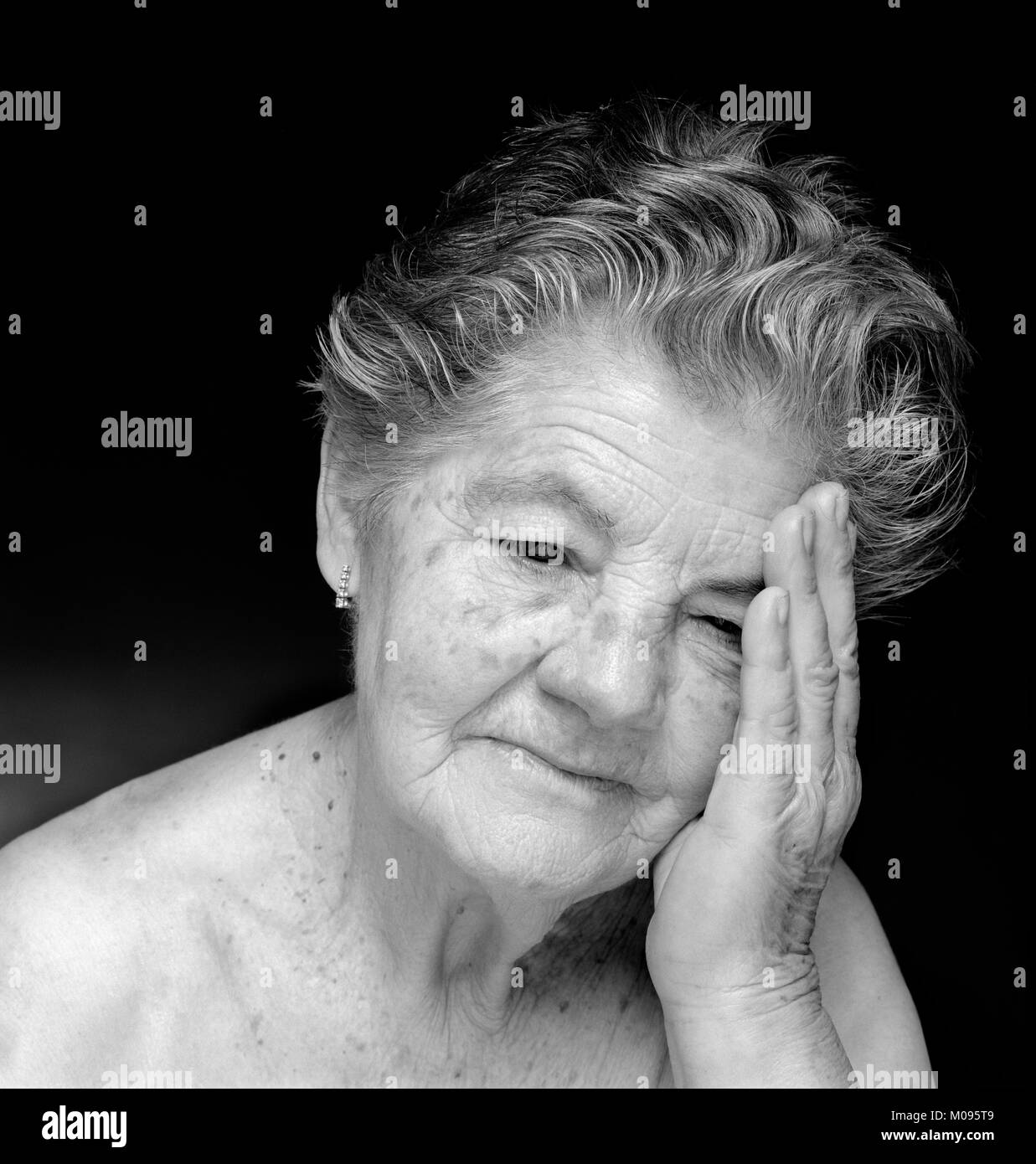 Black and white portrait of melancholic and meditative elderly woman against black background Stock Photo