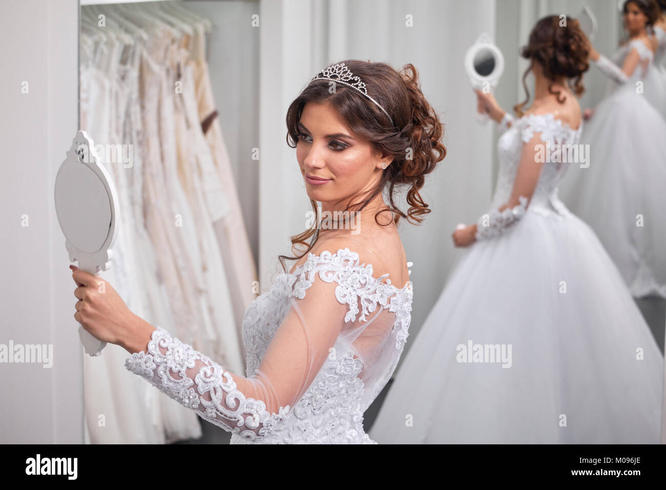 one young bride, looking at self in mirror, bridal salon, wearing gown. Stock Photo