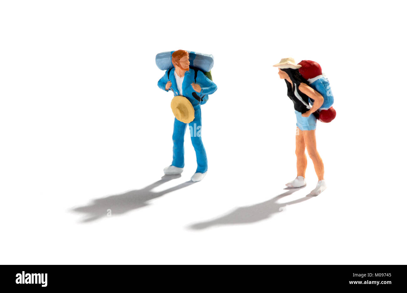 Miniature figures of two travellers or backpackers on a white background with shadows standing looking at each other in a concept of vacations, travel Stock Photo