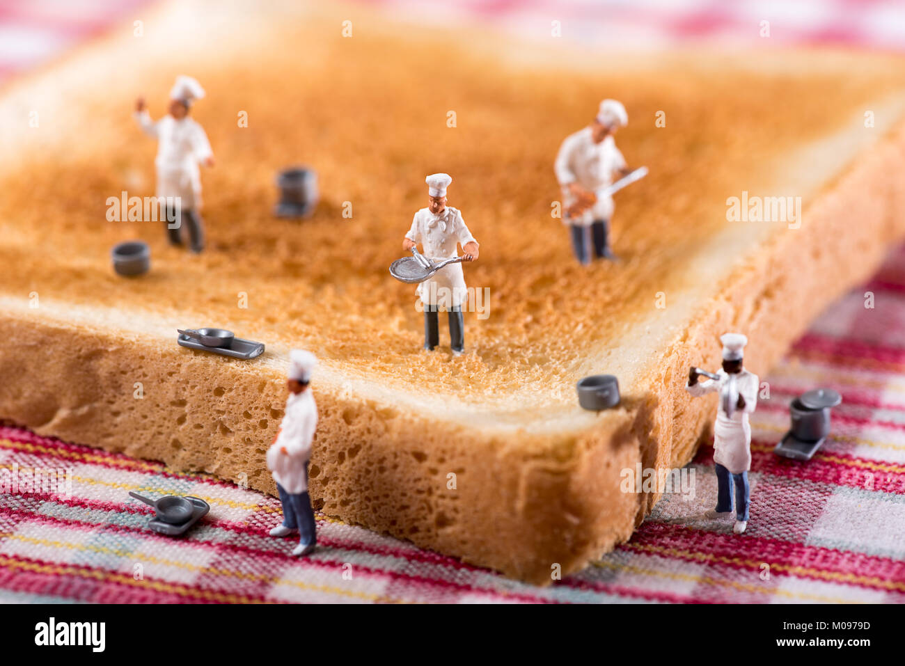 Group of miniature cooks or chefs on a slice of white toast in a concept of teamwork in preparing food and catering Stock Photo