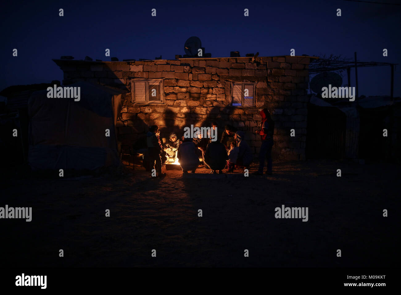 A Palestinian family gather around fire outside their house, to stay ...