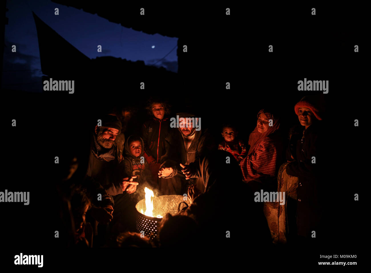 A Palestinian family gather around fire outside their house, to stay ...