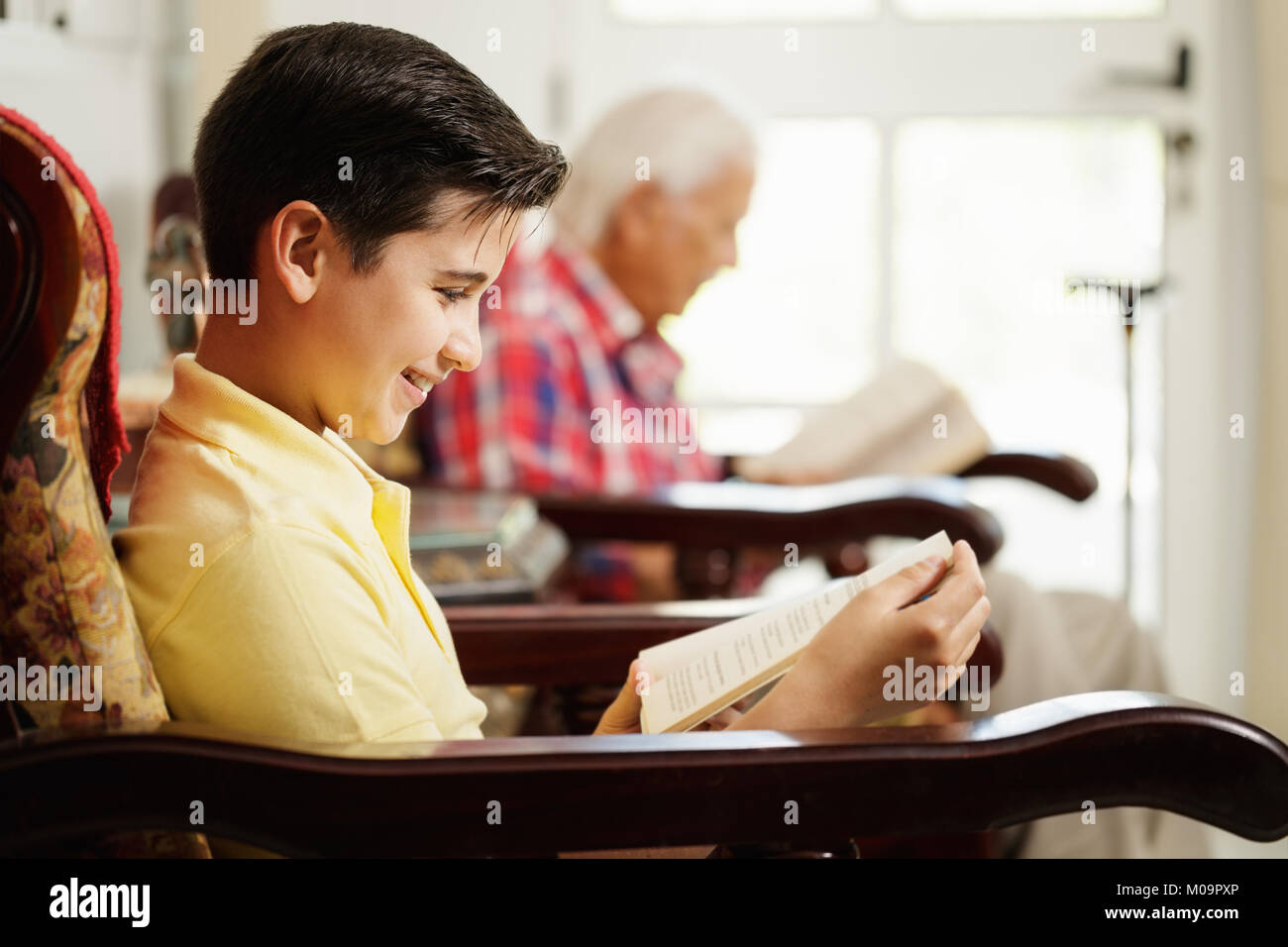 Grandson And Grandpa Reading Book And Relaxing At Home Stock Photo