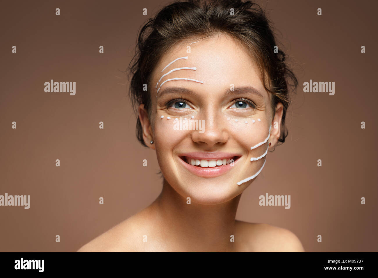 Face lifting. Smiling girl with rejuvenating cream on her face on brown background. Skin care and beauty Stock Photo