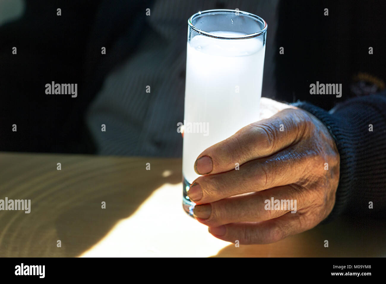 A hand of a senior man holding a glass with ouzo, indoors, natural light, selective focus. Stock Photo