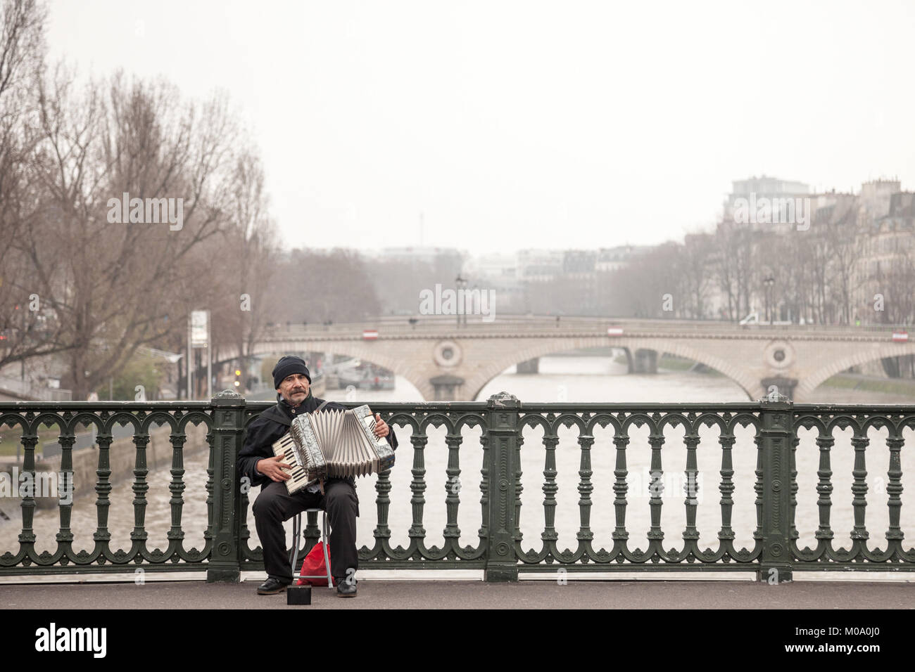 PARIS, FRANCE - DECEMBER 20, 2017:  Accordionist plating accordion on the Arcole bridge in Paris, over the Seine river. Accordion music is supposed to Stock Photo