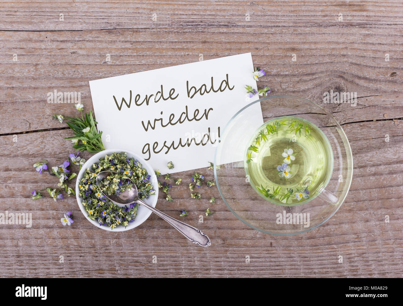 Greeting card with a cup of tea with dried and fresh Viola and white card with german text: get well soon Stock Photo