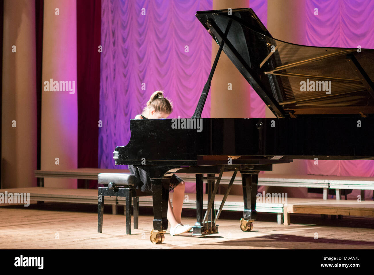 Little girl is playing on a big black piano Stock Photo