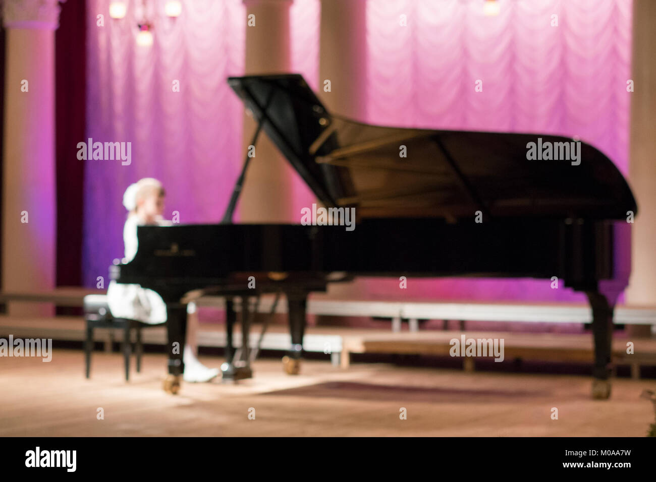 Little girl is playing on a big black piano. Blurry Stock Photo