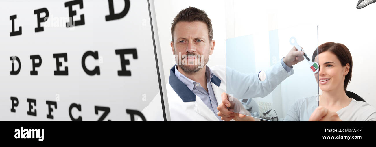 optometrist examining eyesight, woman patient pointing chart at the hole on plexiglass, ocular dominance test Stock Photo