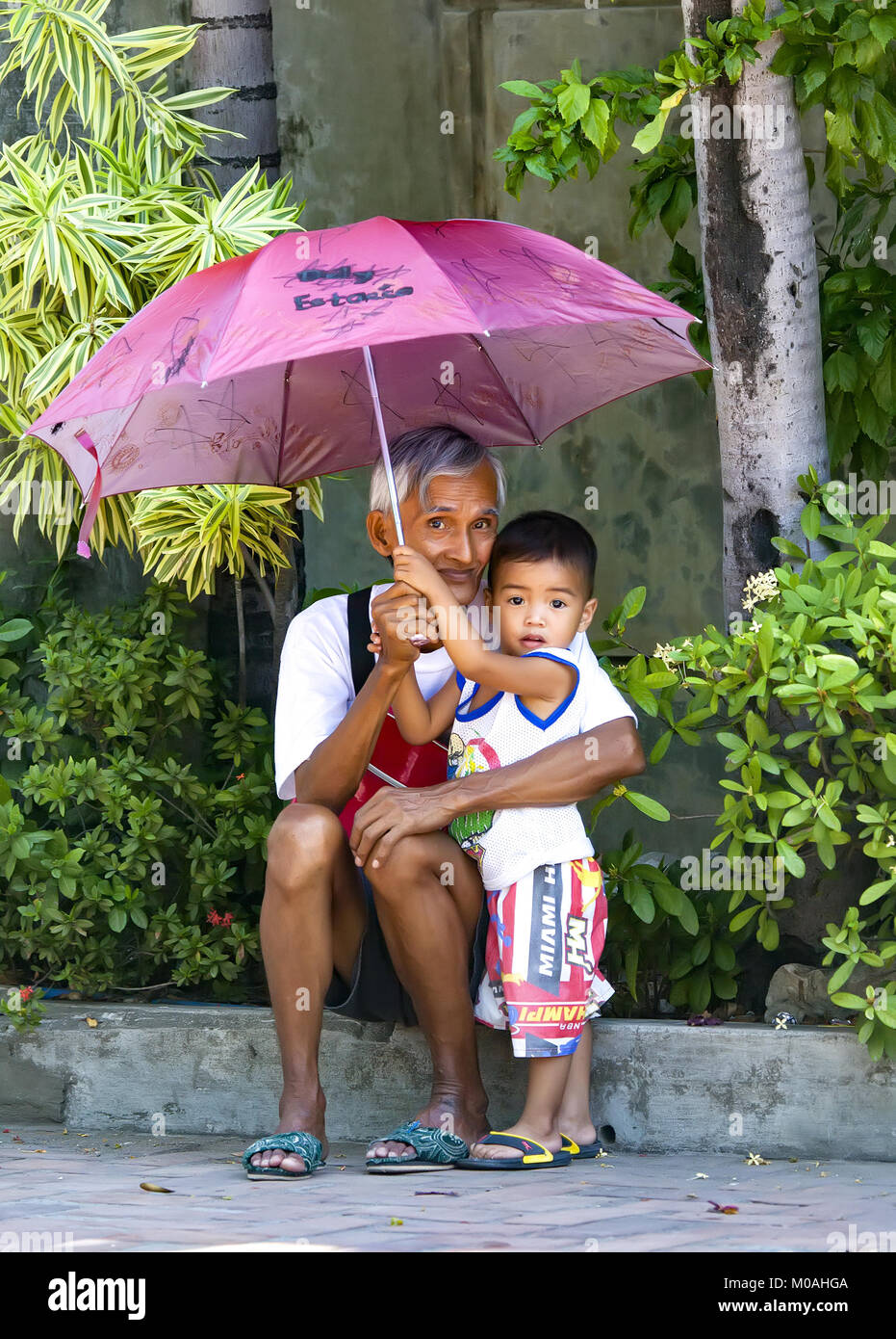 Portrait of a loving Filipino grandfather holding an umbrella over the head of his young grandson at Agoo, Luzon, Philippines. Stock Photo