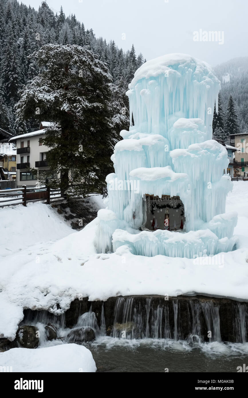 The frozen fountain in the piazza of Canazei in the Val di Fassa, with a central Christmas scene within it. Wooded slopes of the Dolomite mountains be Stock Photo