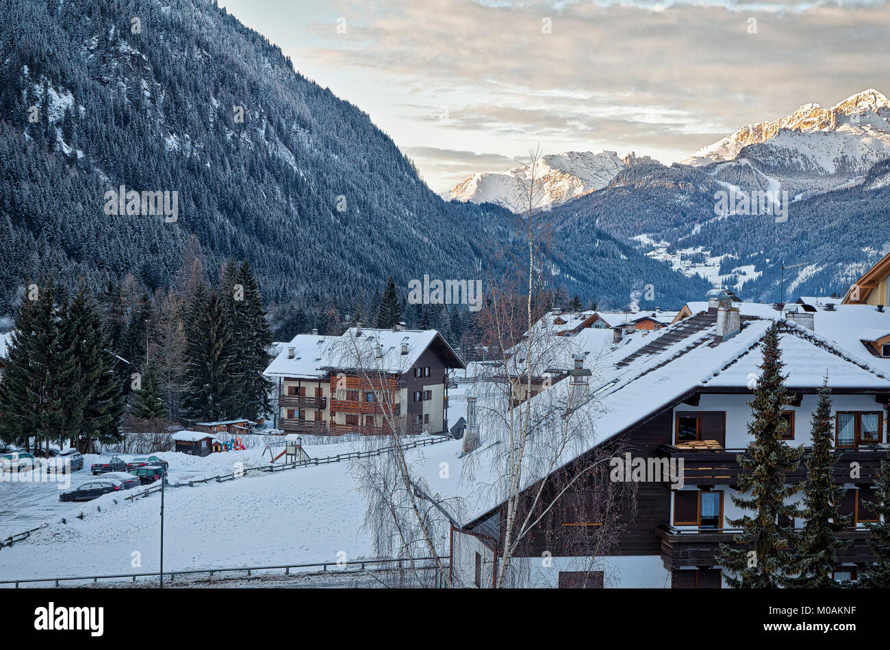 View along the valley at the village of Campitello, with chalets and wooded slopes in the foreground, and the sun catching the distant mountains. Val  Stock Photo