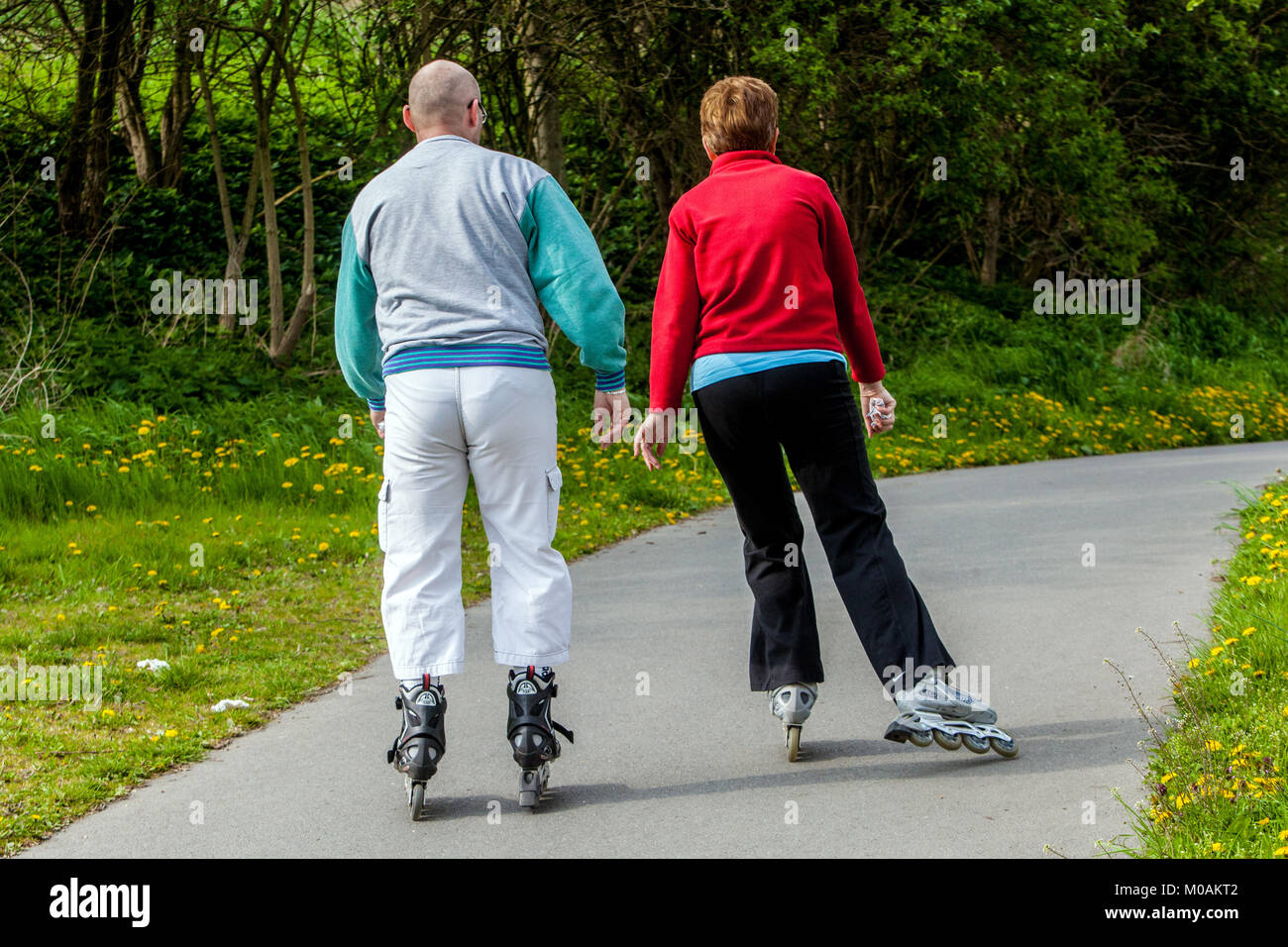 Active seniors inline skating garden path, Active aging Stock Photo