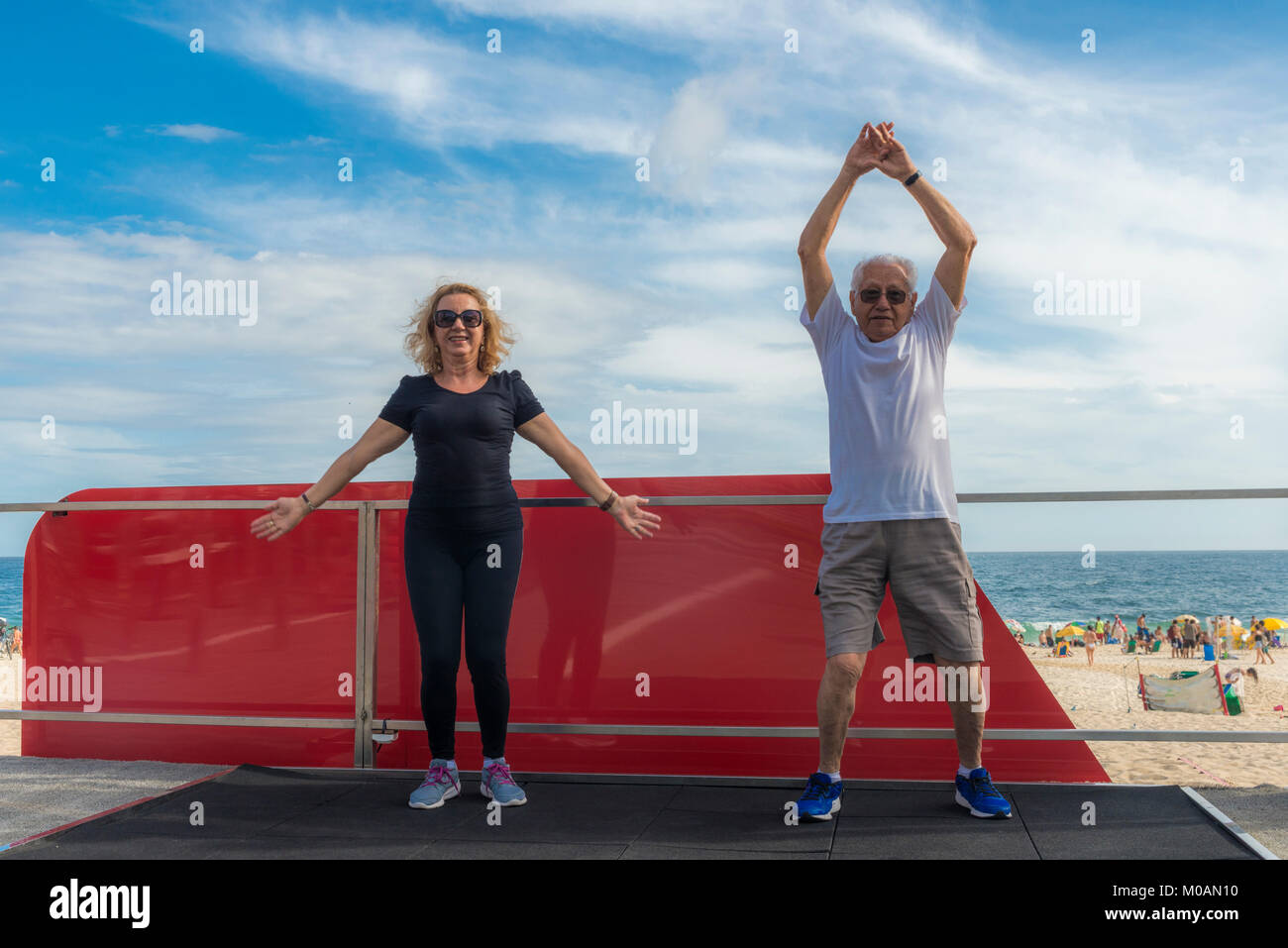 Model Released: Mature man and woman perform jumping jacks at outdoors exercise area near a beach - boot camp Stock Photo