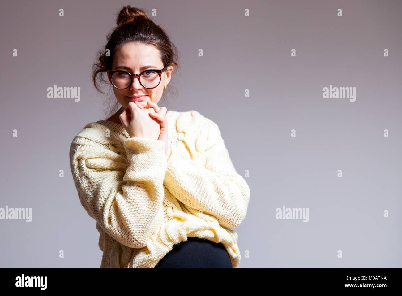 Portrait of a young dark-haired beautiful woman in her late pregnancy with glasses and a knitted milk-colored sweater on a white isolated background Stock Photo